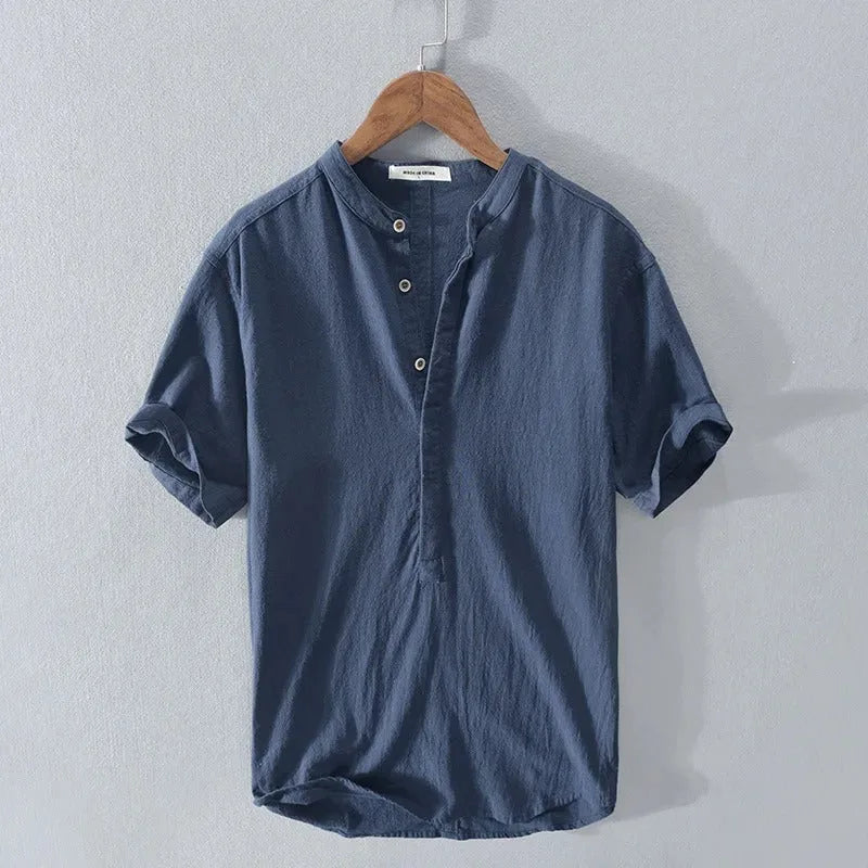Navy blue linen-cotton blend short-sleeve shirt with button placket, hanging on a wooden hanger against a grey wall