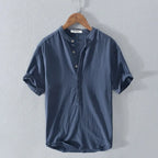 Navy blue linen-cotton blend short-sleeve shirt with button placket, hanging on a wooden hanger against a grey wall