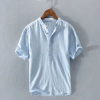 Sky blue collarless short-sleeve shirt with wooden-tone buttons, shown hanging with a relaxed, lightly textured fabric