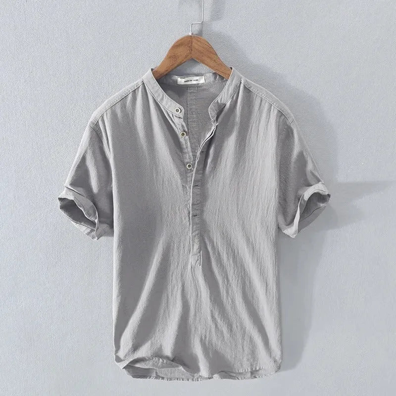 Grey short-sleeve shirt with stand collar and rolled cuffs, hanging on a wooden hanger showing the relaxed fit
