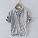 Grey short-sleeve shirt with stand collar and rolled cuffs, hanging on a wooden hanger showing the relaxed fit