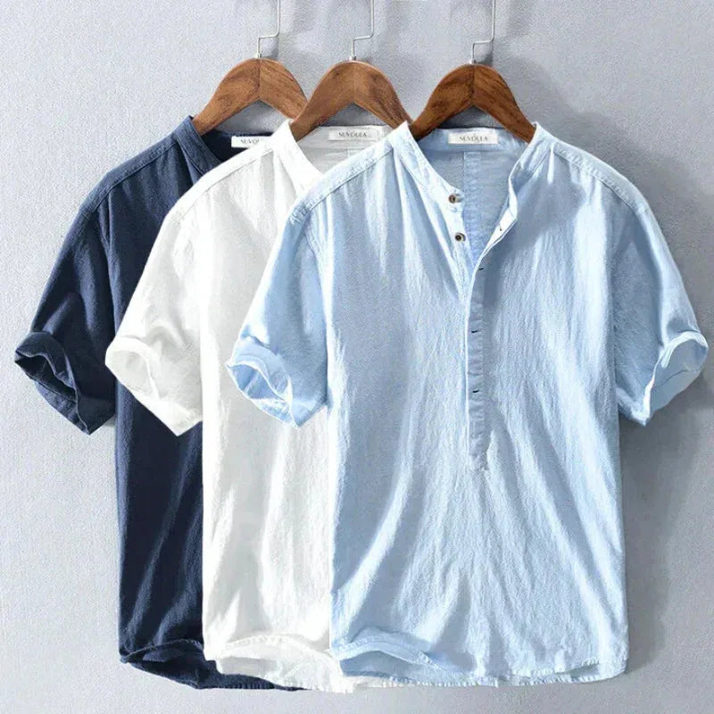 Three shirts in navy, white and sky blue hanging side by side, showing the full colour range of the collarless style