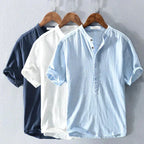 Three shirts in navy, white and sky blue hanging side by side, showing the full colour range of the collarless style