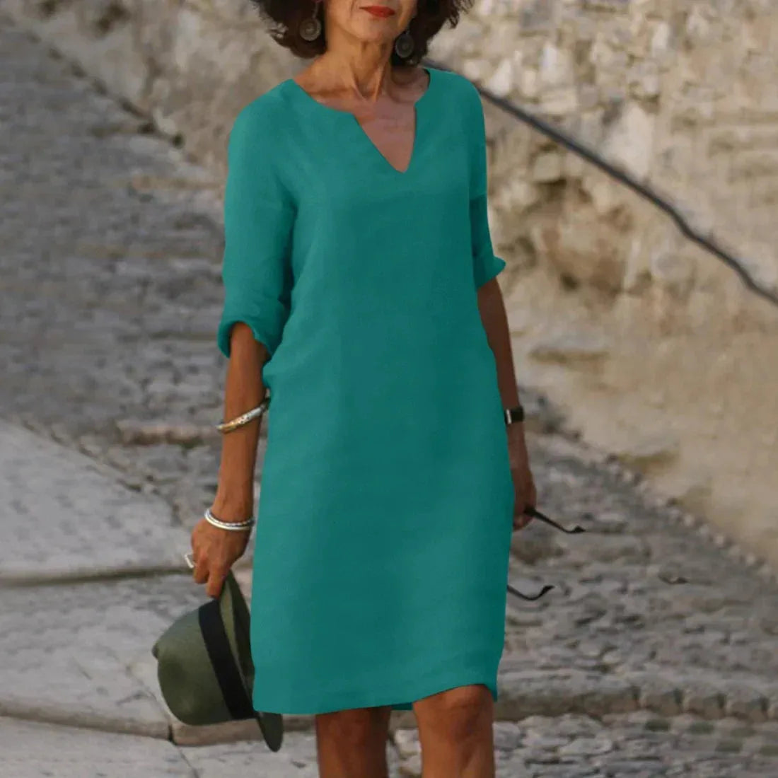Woman wearing a teal linen-look V-neck dress with half sleeves, standing on a cobblestone street