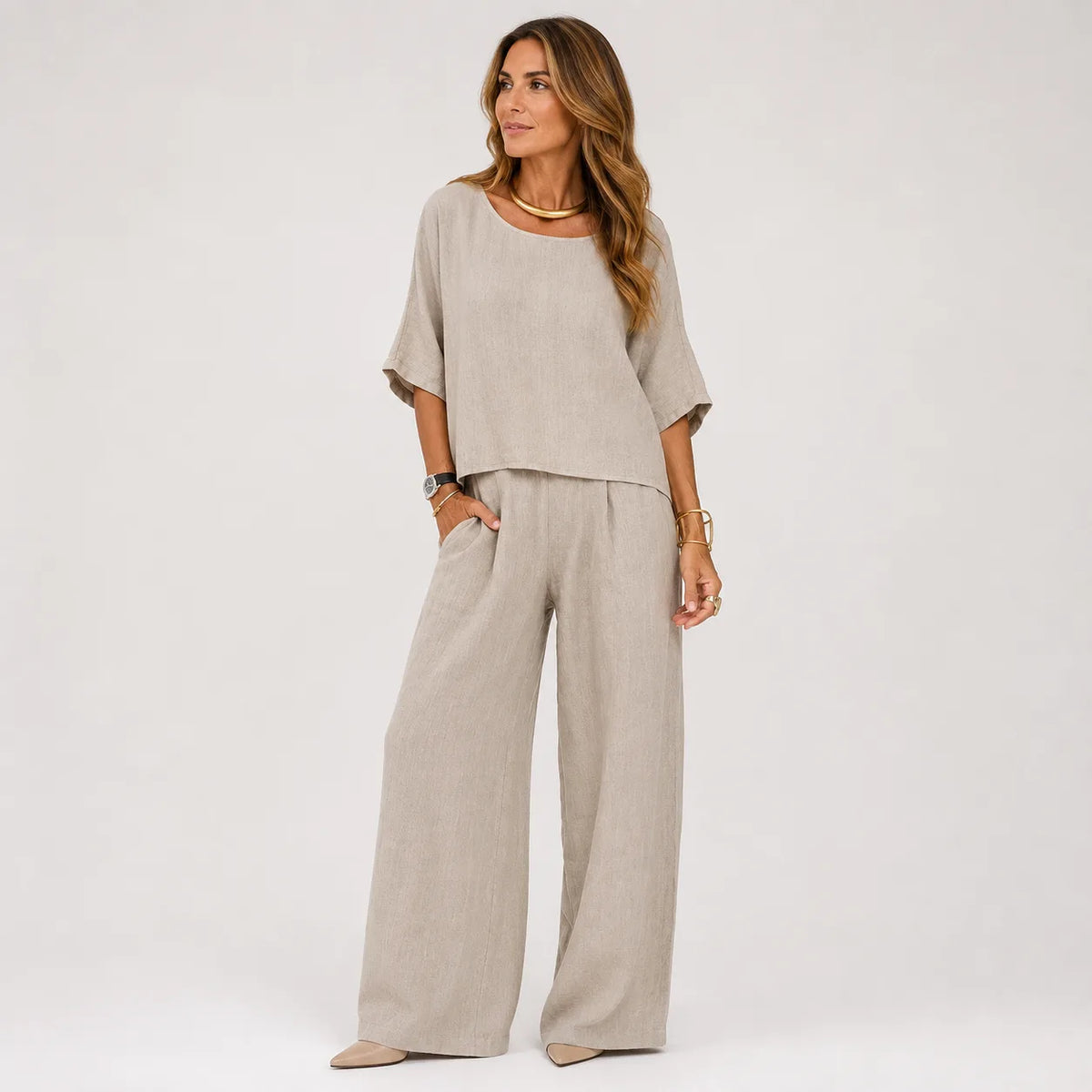 Woman wearing an oversized grey marle linen-look top and wide leg pants set with gold jewellery, styled with pointed flats