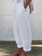 Side view of white linen-look wide-leg trousers with button-tab pocket detail and cuffed hem, paired with sandals