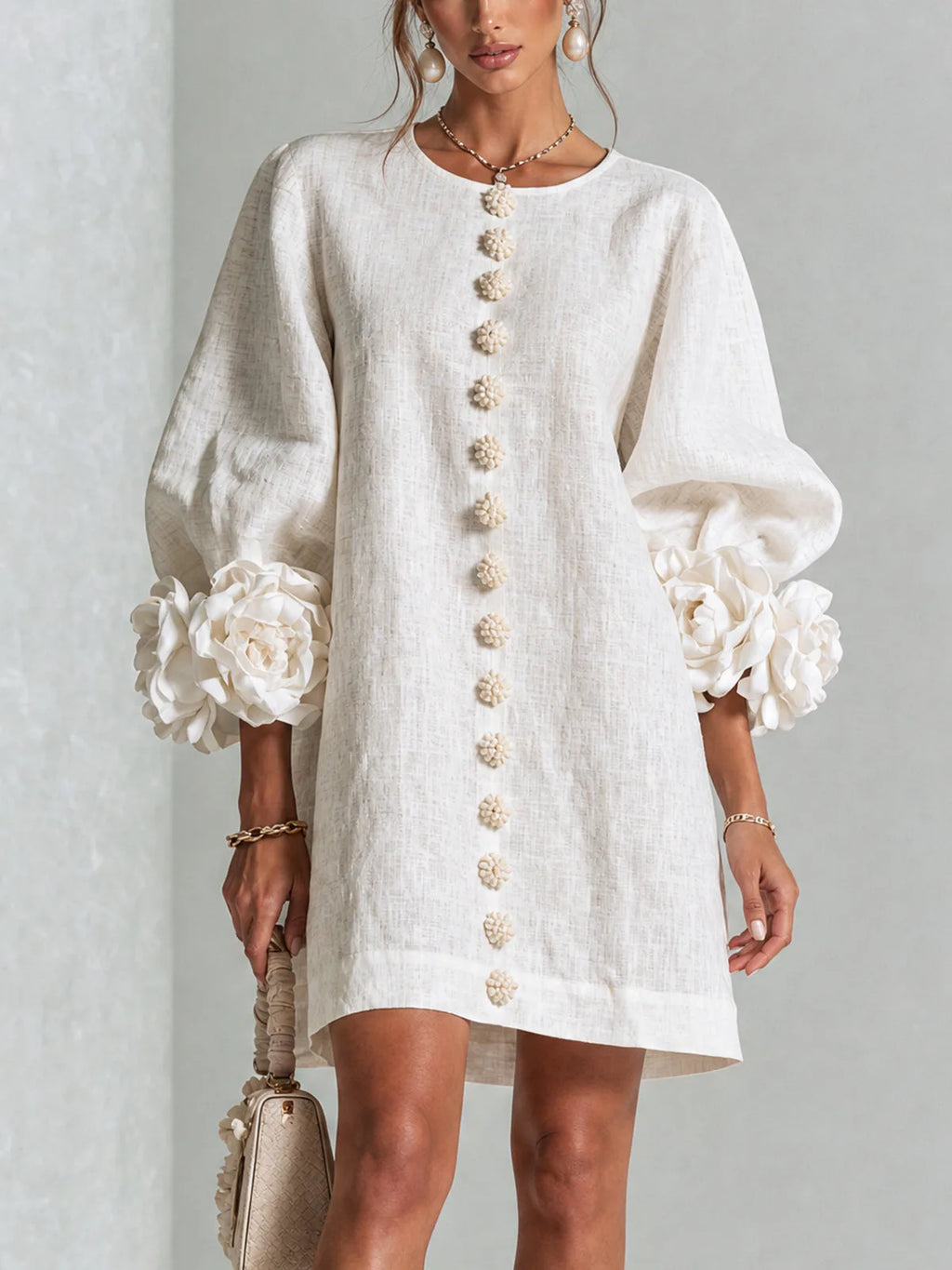 Close-up front view of a woman in a white textured mini dress with 3D floral cuffs and floral button detailing down the front