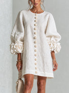 Close-up front view of a woman in a white textured mini dress with 3D floral cuffs and floral button detailing down the front