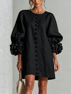 Detail view of the collarless round neckline and top floral button on the white textured dress