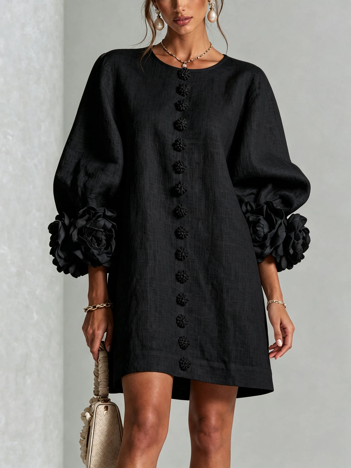 Detail view of the collarless round neckline and top floral button on the white textured dress