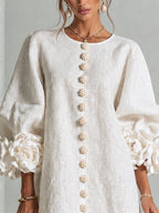 Close-up of the floral-shaped buttons running down the front placket of the white textured dress