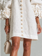 Detail shot of the floral button trim and hemline on the white mini dress, paired with a quilted handbag