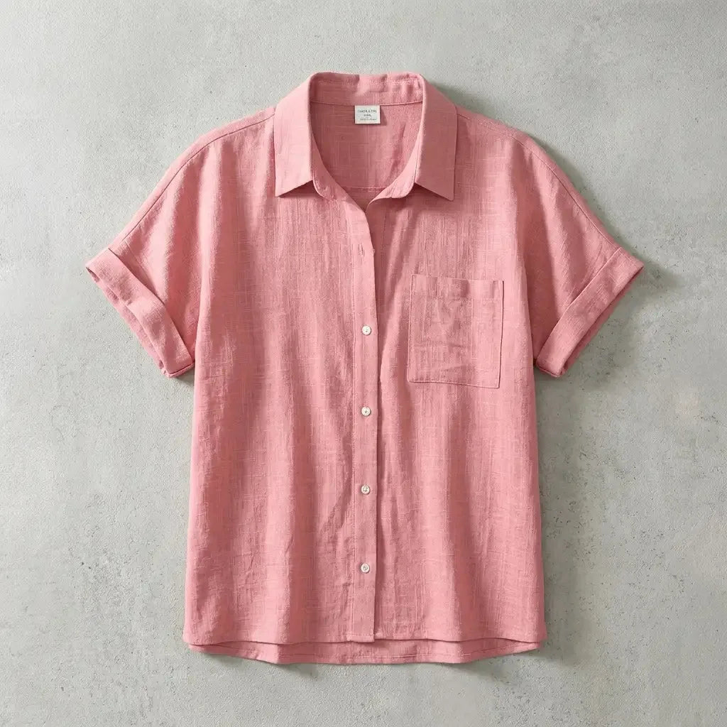 Soft pink linen short-sleeve shirt with chest pocket and rolled cuffs, flat lay on textured grey concrete