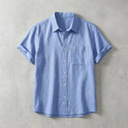 Light blue linen short-sleeve shirt with chest pocket, laid flat showing relaxed collar and button placket