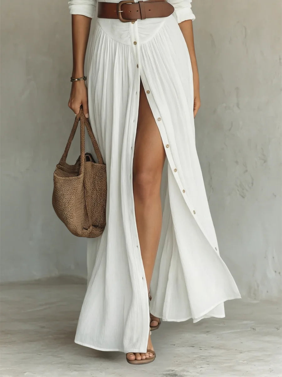 Close-up of the white maxi dress skirt showing pleated button detailing, thigh slit and a woven straw tote bag