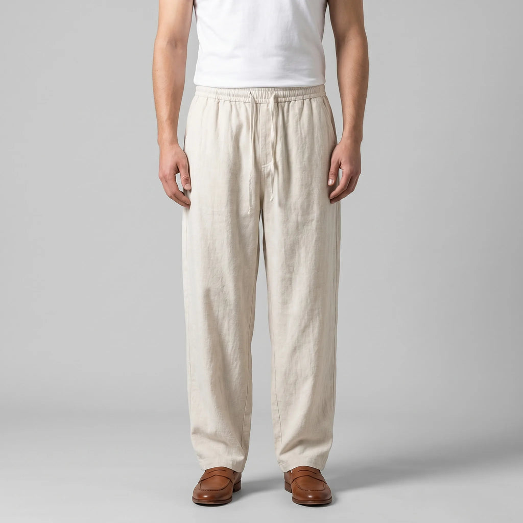 Front view of man wearing beige baggy linen pants with drawstring waist, styled with a white singlet and tan leather loafers
