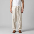Front view of man wearing beige baggy linen pants with drawstring waist, styled with a white singlet and tan leather loafers