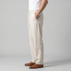Side profile of the beige linen trousers showing the relaxed, wide leg fit and elastic drawstring waistband