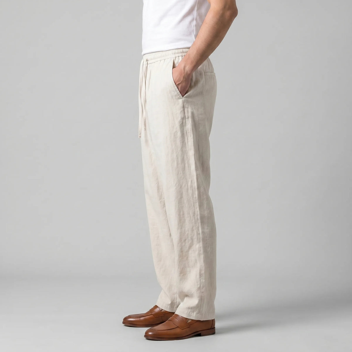 Side profile of the beige linen trousers showing the relaxed, wide leg fit and elastic drawstring waistband