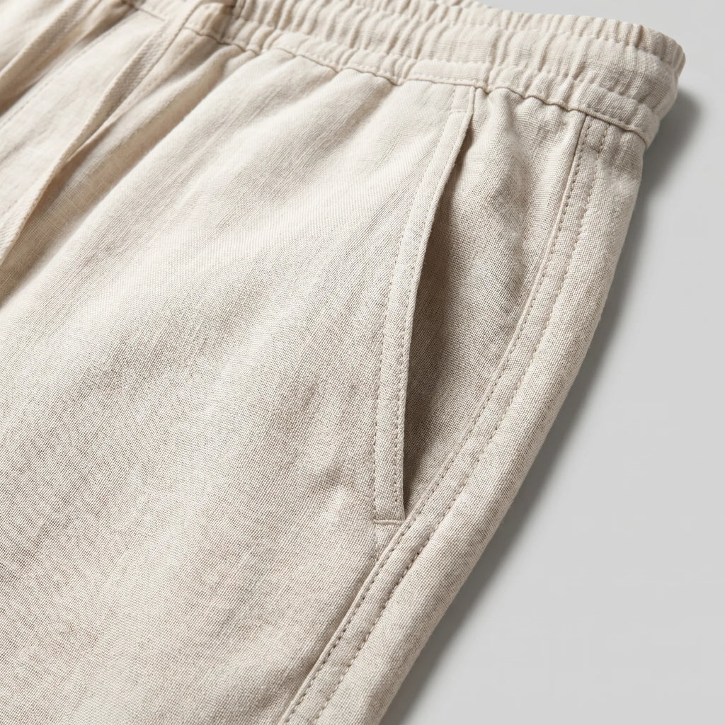 Close-up detail of the linen fabric texture, side pocket and elastic waistband stitching on the beige trousers