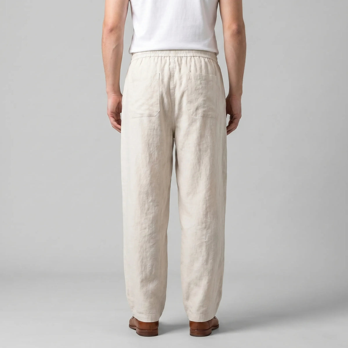 Back view of the beige linen pants showing the relaxed fit, back pocket and straight hem falling above the shoes