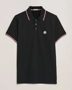 Black polo shirt with ribbed red, white and navy tipped collar and cuffs, logo patch on chest, laid flat