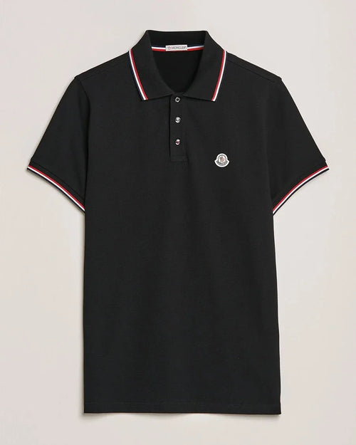 Black polo shirt with ribbed red, white and navy tipped collar and cuffs, logo patch on chest, laid flat