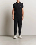 Model wearing a black tipped-collar polo with black tailored pants and white sneakers, full length front view