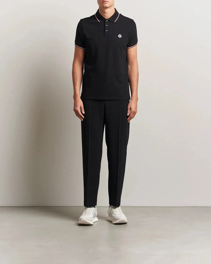 Model wearing a black tipped-collar polo with black tailored pants and white sneakers, full length front view