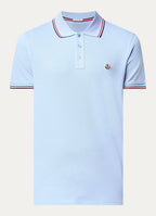 Light blue polo shirt with red, white and navy tipped collar and cuffs and a round logo patch, laid flat