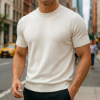 Close-up of a man wearing a cream white short-sleeve knitted T-shirt with ribbed crew neck on a city street