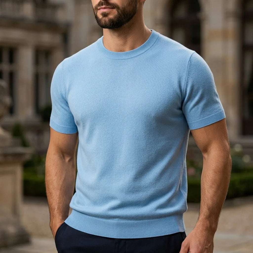 Man in a light blue short-sleeve knit top with ribbed cuffs and hem, standing in front of a stone building