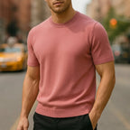 Close-up of a dusty pink short-sleeve knitted T-shirt with ribbed crew neck and cuffs on a city street