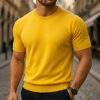 Man wearing a mustard yellow short-sleeve knit T-shirt with ribbed hem on a cobblestone street