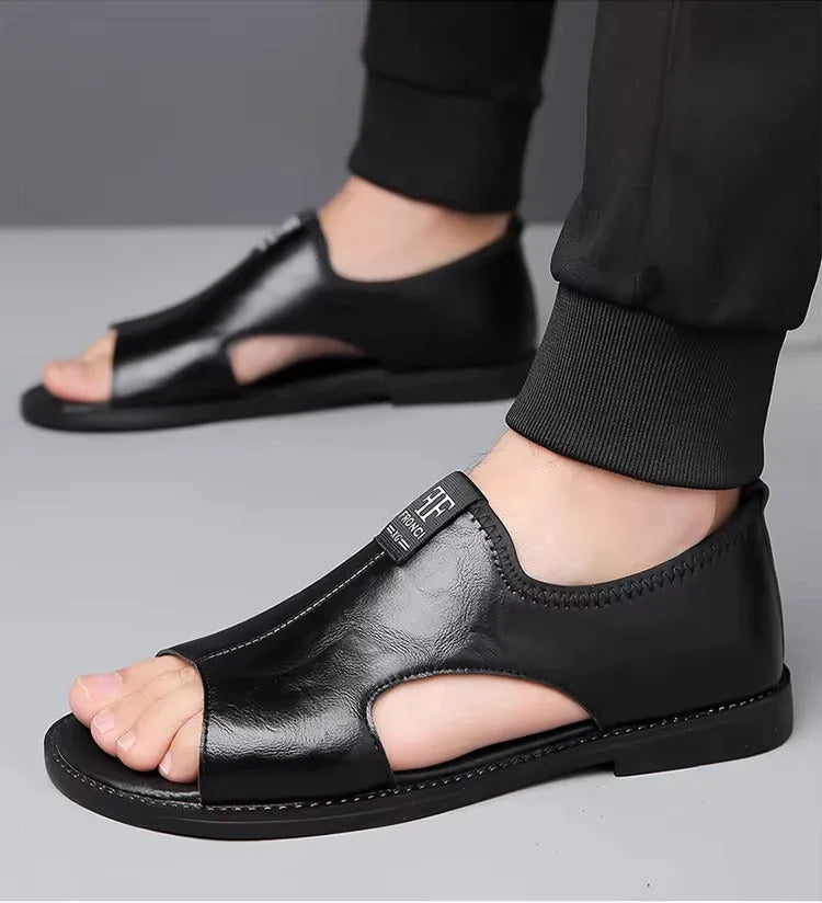Black leather sandal worn on foot with black trousers, showing open-toe and side cutout detail.