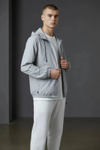 Side profile of a man wearing a grey hooded windbreaker jacket over a white tee, holding the open zip.