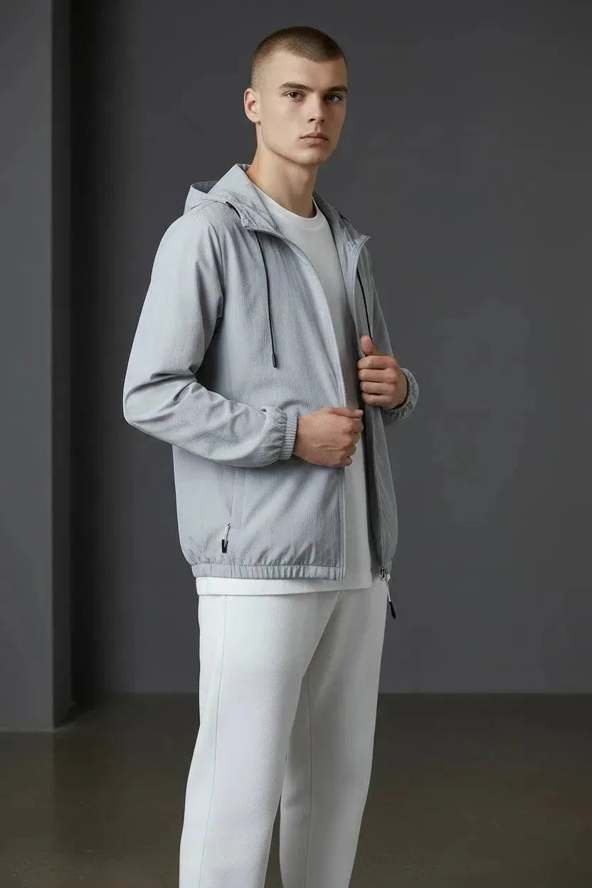 Side profile of a man wearing a grey hooded windbreaker jacket over a white tee, holding the open zip.