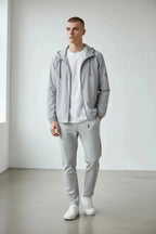 Full front view of the grey hooded windbreaker jacket worn open over a white tee with grey trackpants and sneakers.