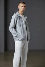 Close-up front angle of the grey windbreaker jacket showing the drawcord hood, zip pockets and elasticated hem.