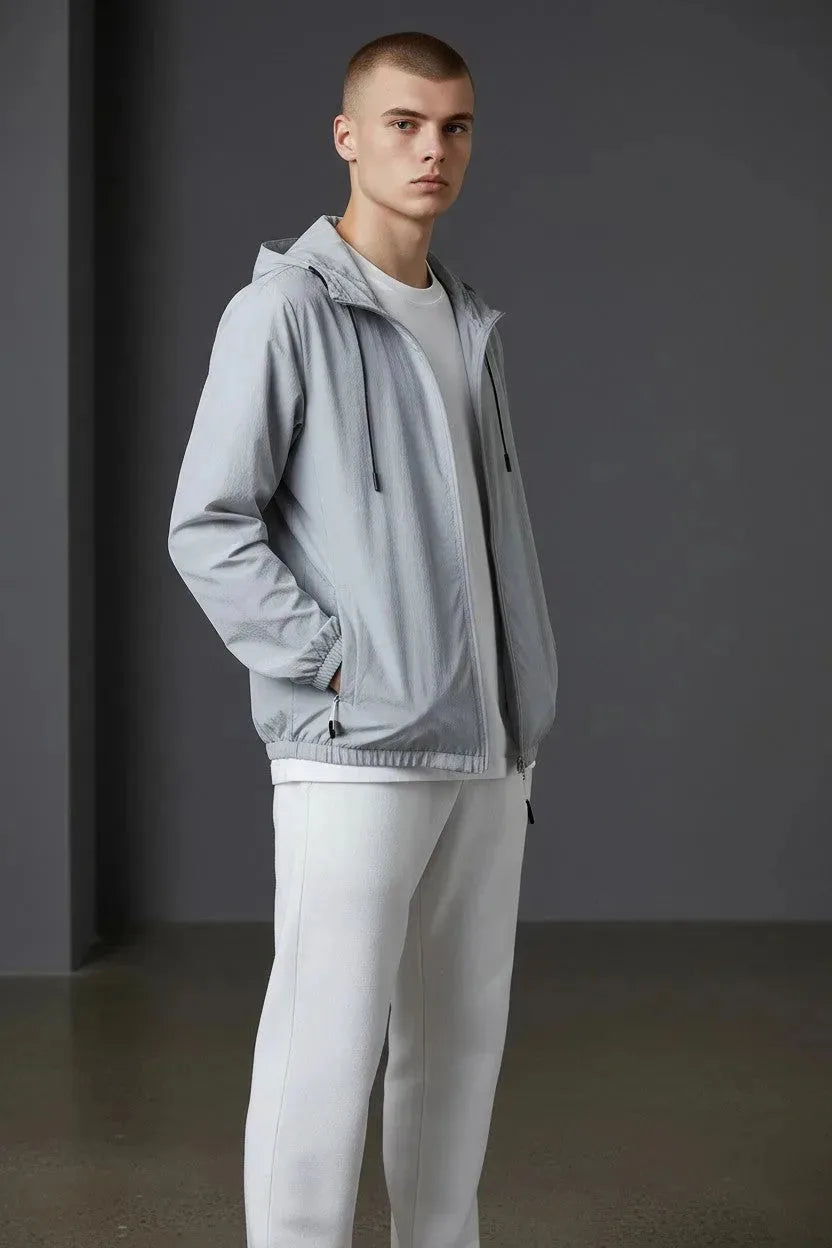 Close-up front angle of the grey windbreaker jacket showing the drawcord hood, zip pockets and elasticated hem.