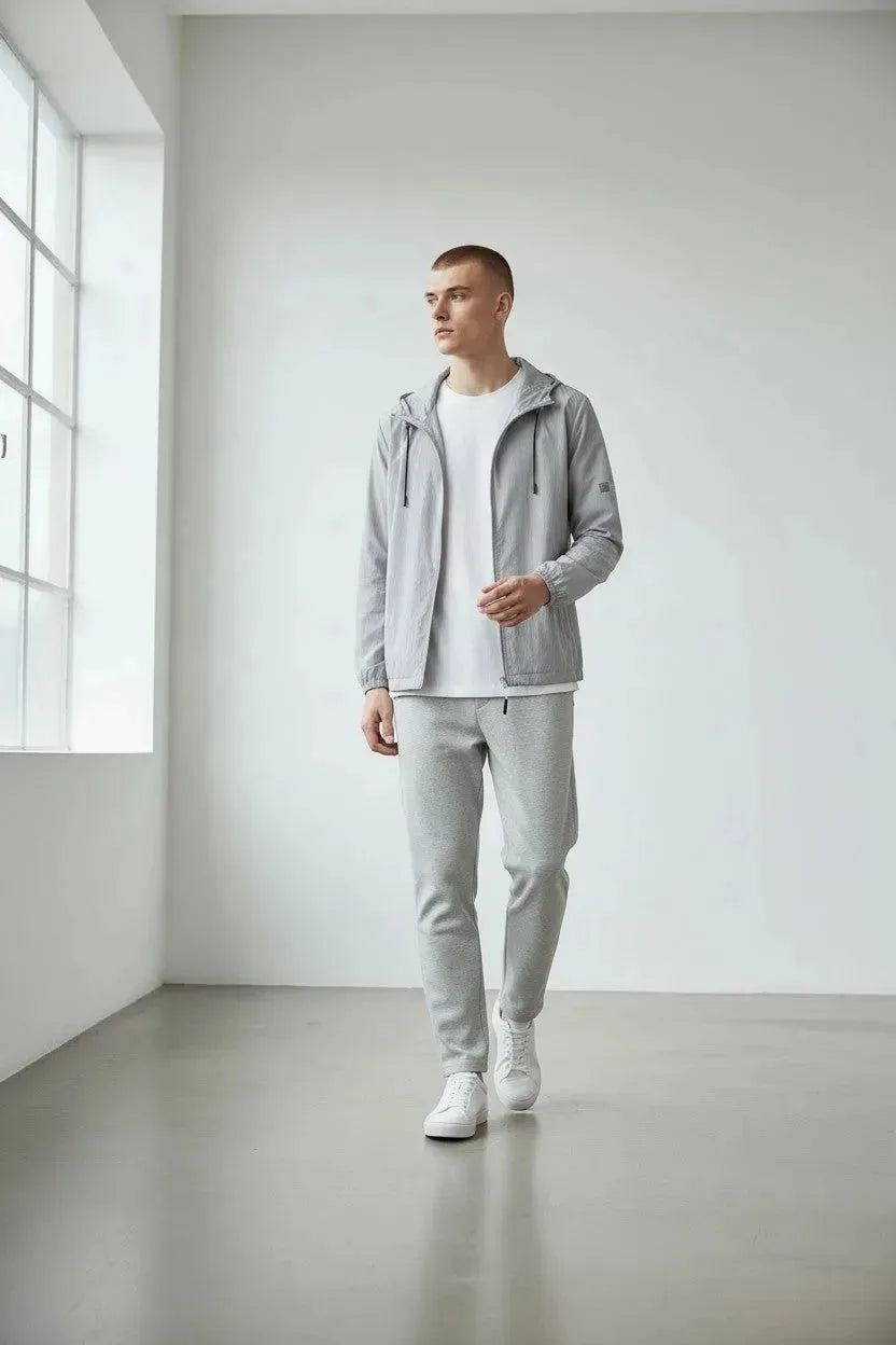 Man walking in the grey hooded windbreaker jacket paired with a white tee, grey trackpants and white sneakers.