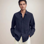 Front view of a navy linen long-sleeve shirt worn open at the collar over white pants, model facing camera