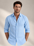 Man wearing a light blue linen-look button-up shirt with sleeves rolled, worn open-neck over the chest, front view
