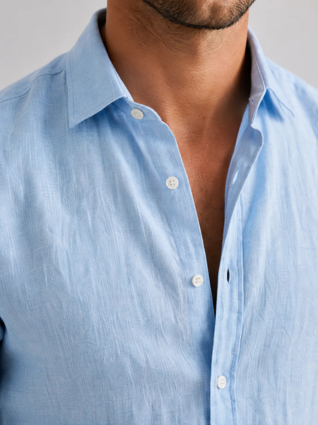 Close-up of the light blue linen-look shirt collar and button placket showing the woven texture of the fabric