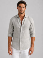 Man wearing a light grey linen-look button-up shirt with rolled sleeves, buttoned down over white trousers