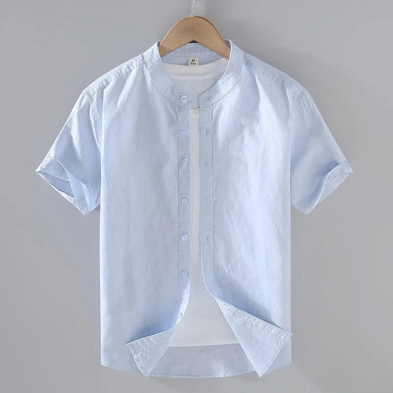 Pale blue linen short sleeve shirt on a hanger, shown with stand collar and rounded hem open over a white tee