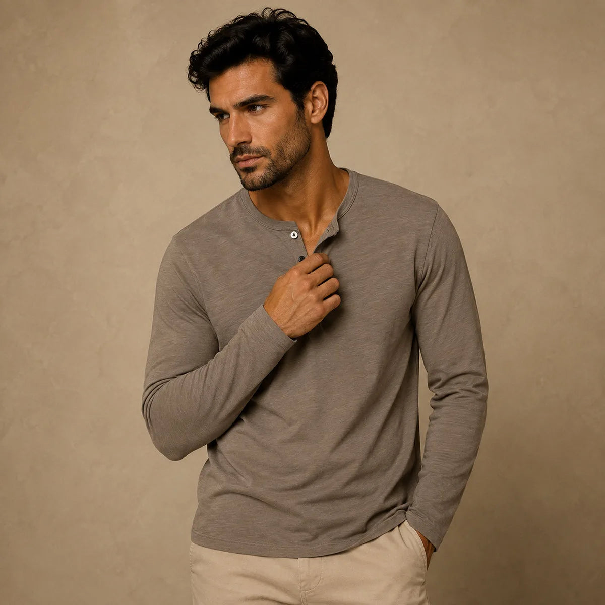 Man wearing khaki brown henley shirt, holding collar open, paired with beige chinos