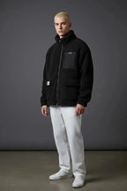 Side angle showing relaxed oversized fit of black sherpa jacket with flap pockets and woven brand patch