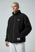 Close-up of black sherpa fleece jacket zipped up, highlighting stand collar and chest logo detail