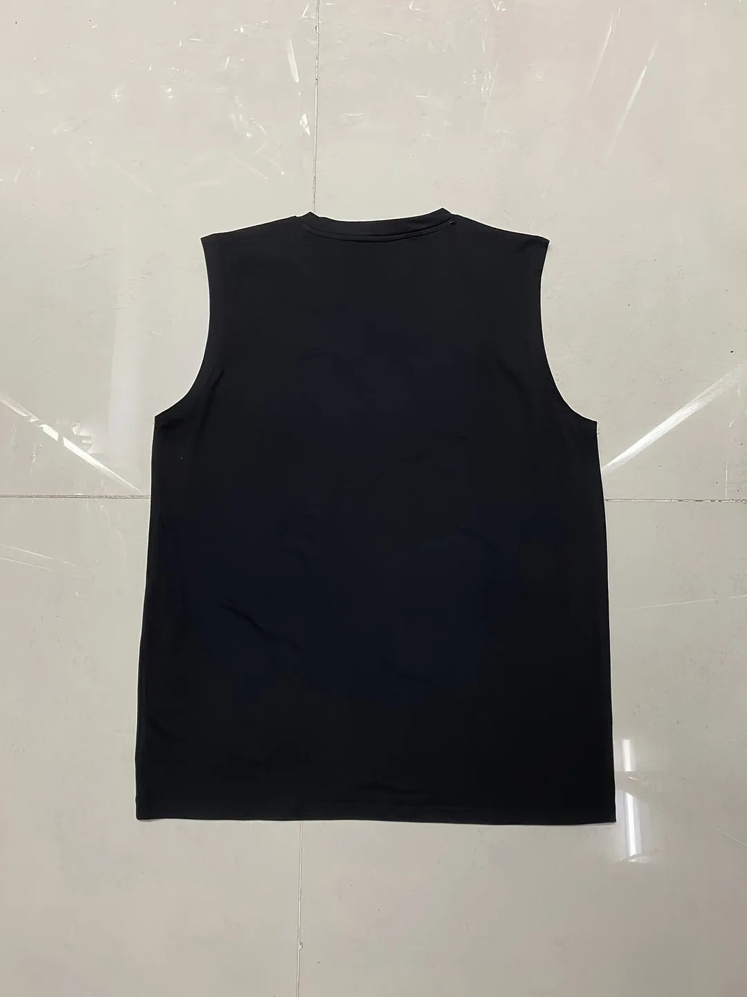 Flat lay of a black sleeveless tank top on a tiled floor showing the crew neckline and overall silhouette